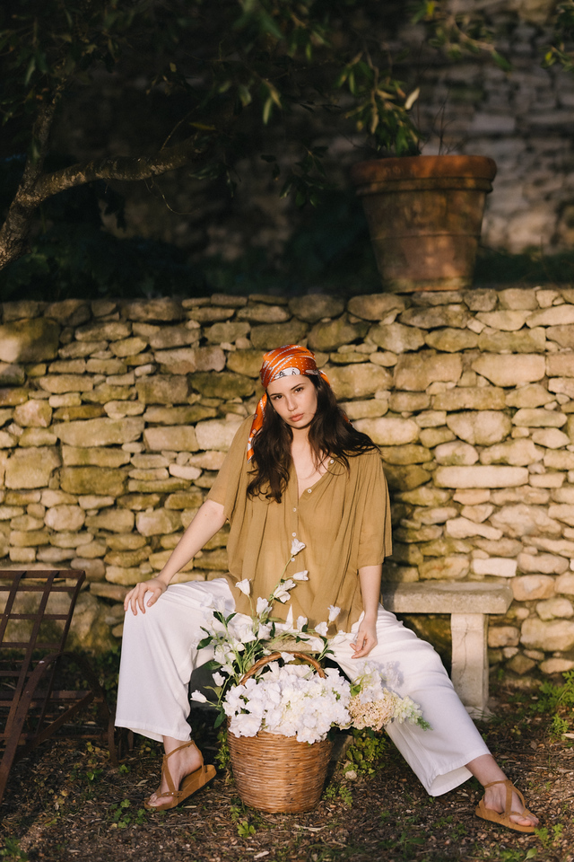 Marlo — blouse kaki et pantalon blanc, mur en pierres sèches